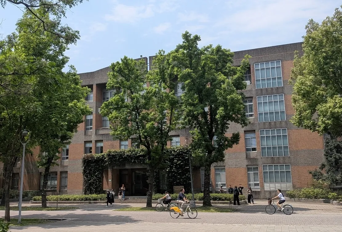 cyclists outside a large school building surrounded by trees