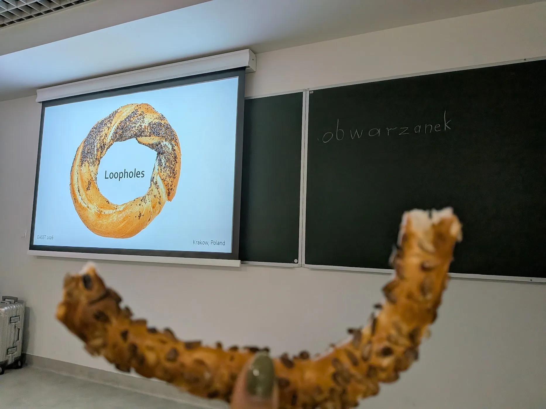 a bread held up in front of a classroom chalk board and digital presentation